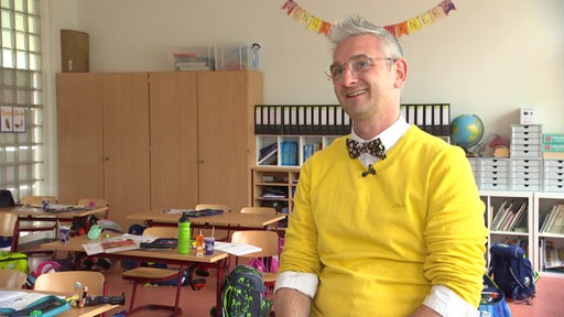 Dirk Buchmann sitzt im Klassenraum und lacht.