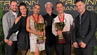 Das Tanzpaar Luna Albanese und Dimitri Kalistov vom Bremer Grün-Gold-Club posiert mit ihren goldenen Pokalen in der Hand nach dem Gewinn der Jugend-EM in Tallinn neben Uta und Roberto Albanese und dem GGC-Vorsitzenden Jens Steinmann.