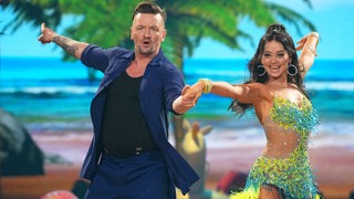 Profi-Tänzerin Malika Dzumaev vom Bremer Grün-Gold-Club tanzt in einer bunten, tropischen Kulisse der Show "Let's Dance" mit dem Musiker Ben Zucker einen Cha-Cha-Cha.
