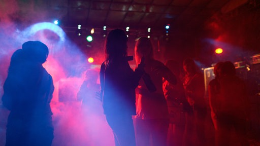 Menschen tanzen in einer Disko bei buntem Scheinwerferlicht.