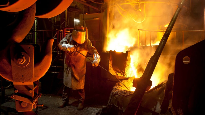 Ein Arbeiter steht in einer Metallgießerei an einem Schmelzofen.