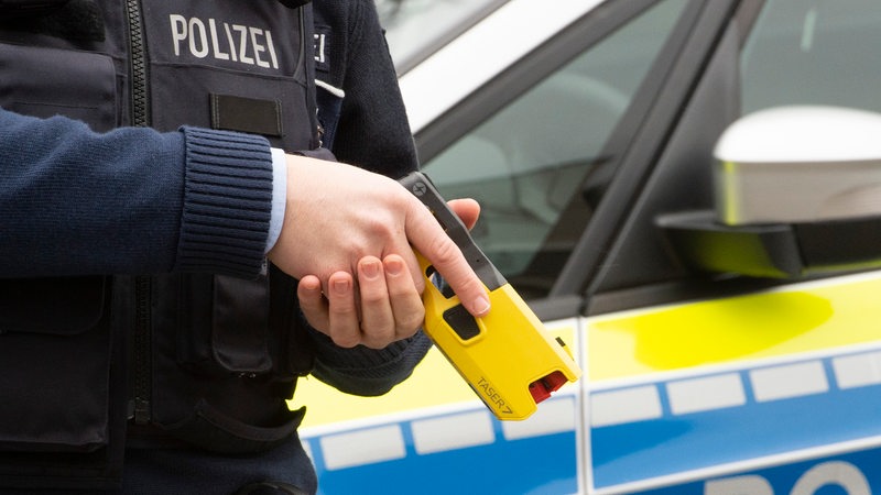 Ein Polizist hält einen gelben Taser in der Hand.