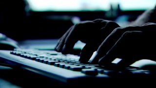 Schattige Hände tippen in einem dunklen Raum auf der Tastatur eines Computers.