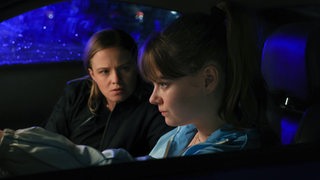 Zwei Frauen sitzen bei Dunkelheit im Auto, der Blick geht auf der Fahrerseite ins Auto.