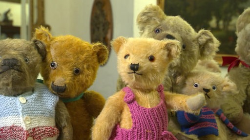 Eine Reihe ausgestellter, alter Teddybären mit Strickkleidung.
