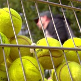 Ein Korb voller gelber Tennisbälle. Dahinter ein Mann mit Cappy im unscharfen Bereich.