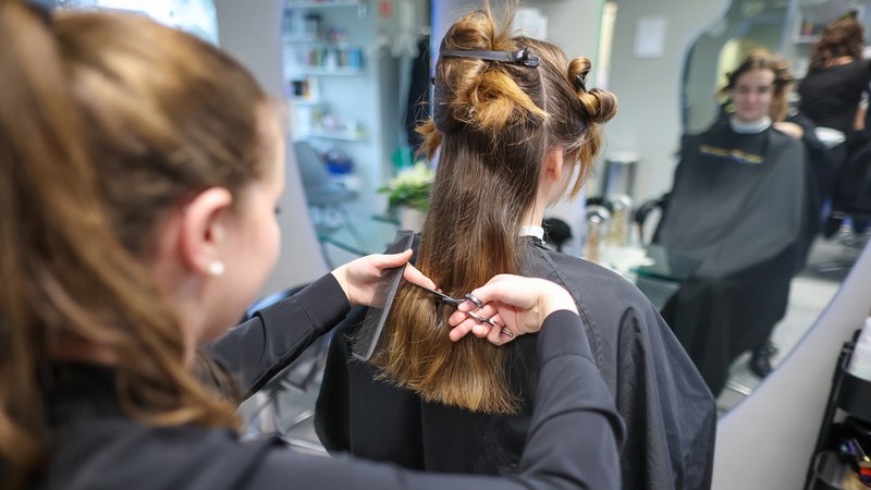 Eine Friseurin schneidet einer Kundin die langen Haare.