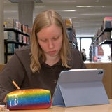 Eine Frau sitzt vor einem Tablet und schreibt.
