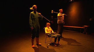 Drei Schauspielerinnen und Schauspieler während einer Inszenierung in einem Theater.