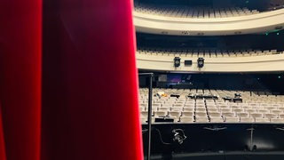 Ein roter, halbzugezogener Vorhang auf der Bühne eines leeren Theaters