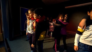 Grundschulkinder stehen auf einer Bühne und umarmen sich.