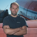 Thomas Krumpen verschränkt die Arme und guckt in die Kamera. Im Hintergrund sind Teile eines Forschungsflugzeugs zu sehen.