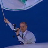 Thomas Schaaf schwenkt eine Werder-Fahne und hält eine Kamera in der Hand.
