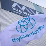 Die Fahne des Unternehmens ThyssenKrupp weht vor der Schiffbauhalle auf dem Gelände der Werft an der der Schriftzug „MV Werften“ zu sehen ist. 