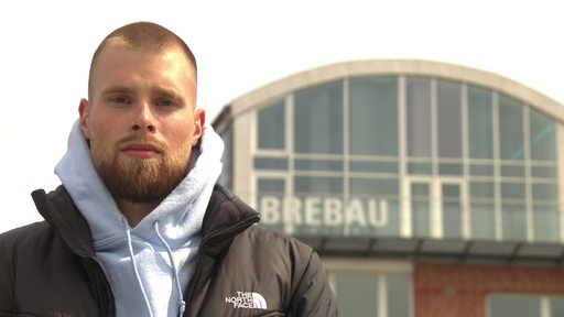 Tim Schoenian, ein junger Mann, steht vor dem Gebäude der Brebau an der Schlachte in Bremen.
