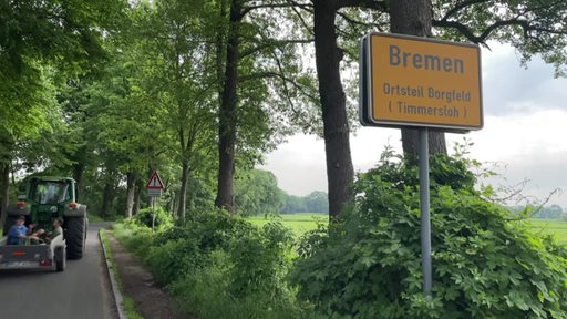 Das Ortsschild von Timmersloh in Bremen Borgfeld. Auf der Landstraße fährt ein Trekker.