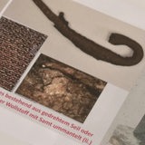 Ein Hornförmiger Gegenstand neben einer Abbildung eines Umhangs, an dem ein solcher Gegenstand oben an der Kaputze befestigt ist. 