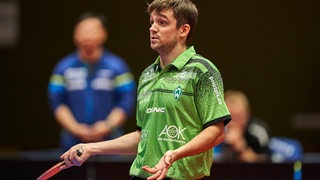 Werders Tischtennis-Profi Kirill Gerassimenko hebt am Tisch fragend die Arme.