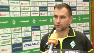 Werders Tischtennis-Trainer Cristian Tamas vor einer Werbewand beim Interview nach dem Spiel.