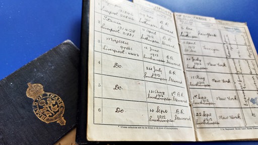 Ein aufgeschlagenes Seefahrtsbuch der Titanic mit handschriftlichen Eintragungen und ein geschlossenes.