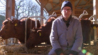 Der Landwirt Tobias Bertzbach sitzt auf Heu, im Hintergurnd seine Kühe. 