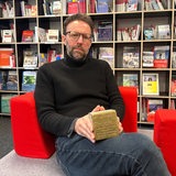 Tobias Peters sitzt in einer Bibliothek und hält einen Stolperstein in den Händen.