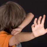 Ein kleiner Junge dreht sich von der Kamera weg und hebt abwehrend die Hand