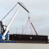 Ein Kran hebt ein Tor aus dem Wasser.