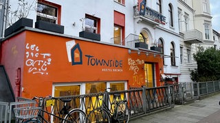 Ein Reihenhaus mit der Aufschrift "Townside Hostel", am Geländer vor dem Hostel sind Fahrräder angeschlossen.