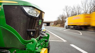 Vor einer Autobahnauffahrt steht ein Traktor.