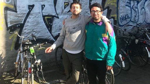 Two men hugging in front of a wall of graffiti