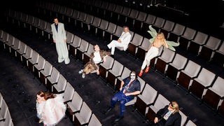 Die Mitglieder des Theater-Ensembles sitzen mit einigem Abstand auf Sitzen im Publikumsbereich.