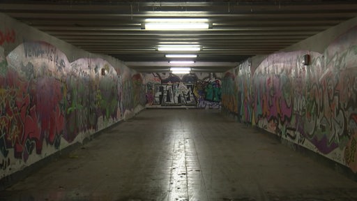Zu sehen ist ein mit Grafittis beschmierter dunkler tunnel.