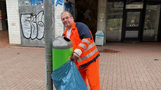 Ein Mann im öffentlichen Dienst entleert einen Mülleimer an einer Haltestelle