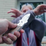 Symbolbild für einen Überfall: Jemand zückt ein Messer, ein Mann kreuzt zum Schutz seine Arme.