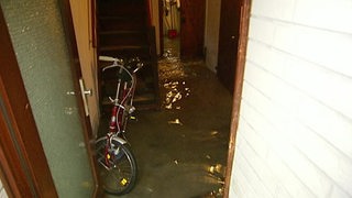 Durch eine offene Tür sieht man einen mit Regenwasser überfluteten Eingangsbereich vom Keller. 