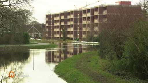 Ein überschwemmter Fluss, im Hintergrund Wohnhäuser.