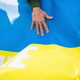 Eine Männerhand ist auf einem Transparent, das die Farben blau und gelb der ukrainischen Nationalflagge hat, zu sehen.