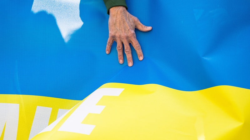 Eine Männerhand ist auf einem Transparent, das die Farben blau und gelb der ukrainischen Nationalflagge hat, zu sehen.