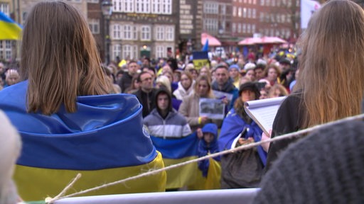 Es sind viele Menschen mit ukrainischen Flaggen, auf dem Marktplatz bei einer Gedenkveranstaltung zu sehen.