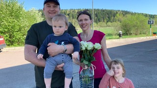 Ein Mann mit Kleinkind auf dem Arm, eine schlanke Frau mit einem jungen Kind an der Hand.