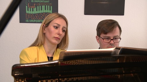Ein Paar sitzt am Klavier und spielt Musik.