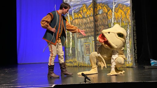 Ein Mann mit Bogen und eine Person als Frosch verkleidet auf der Bühne