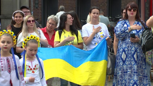 Mehrere Ukrainer halten ihre Flagge hoch und singen ihre Nationalhymne. 