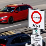Ein Schild weist auf eine Umweltzone hin. Im Hintergrund fährt ein rotes Auto.