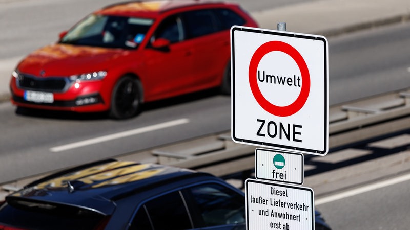 Ein Schild weist auf eine Umweltzone hin. Im Hintergrund fährt ein rotes Auto.