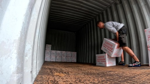 Ein Mann bepackt einen Container mit Umzugskartons.