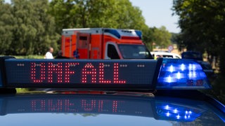 Ein Einsatzfahrzeug der Polizei steht mit Blaulicht und dem Schriftzug Unfall im Display an einem Unfallort
