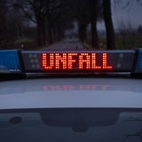 Ein Einsatzfahrzeug der Polizei steht mit Blaulicht und dem Schriftzug "Unfall" im Display auf einer Landstraße.