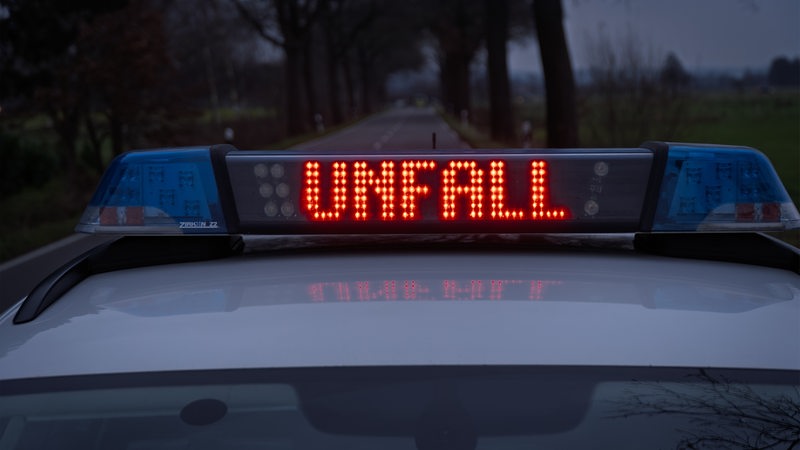 Ein Einsatzfahrzeug der Polizei steht mit Blaulicht und dem Schriftzug "Unfall" im Display auf einer Landstraße.
